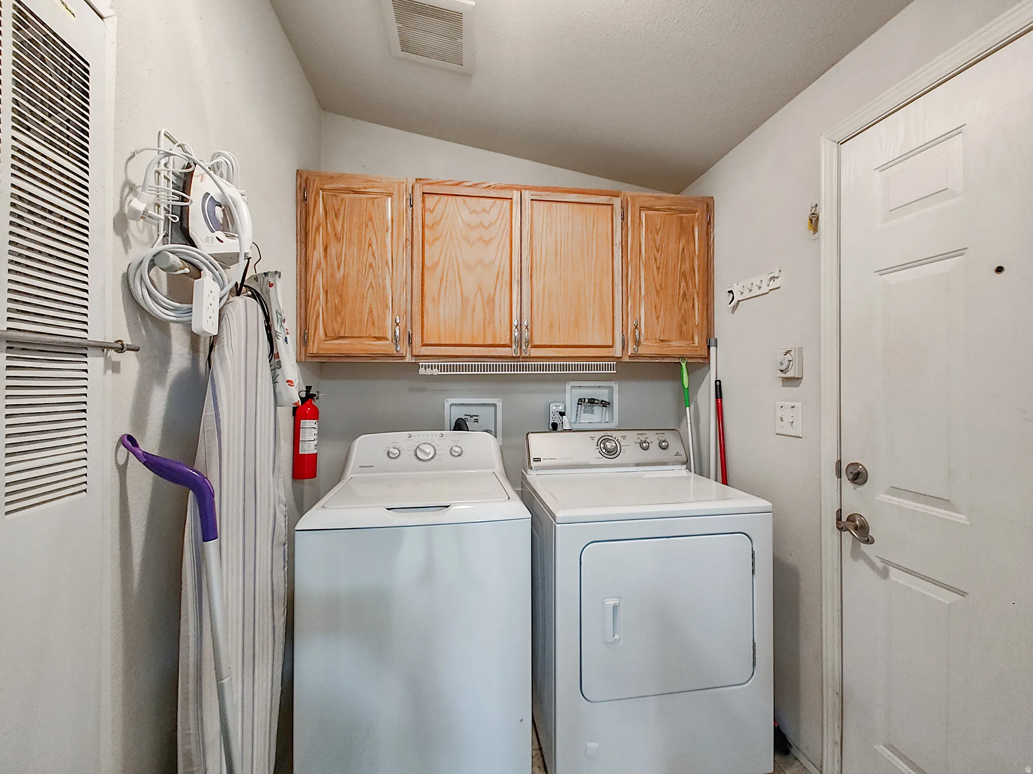 Laundry room and mudroom between backyard entrance and kitchen featuring overhead wood cabinetry and a white paneled door
