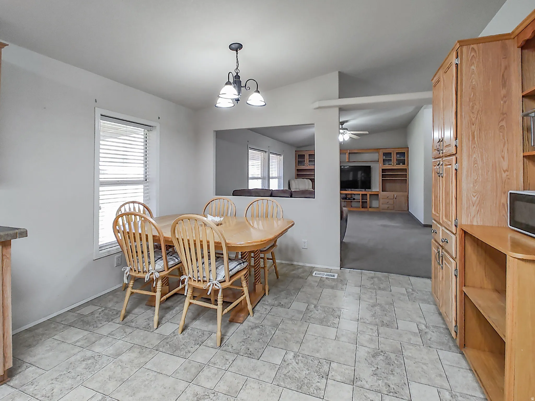 Kitchen dining area featuring neutral-toned tile flooring, a window with blinds, and a chandelier-style ceiling fixture