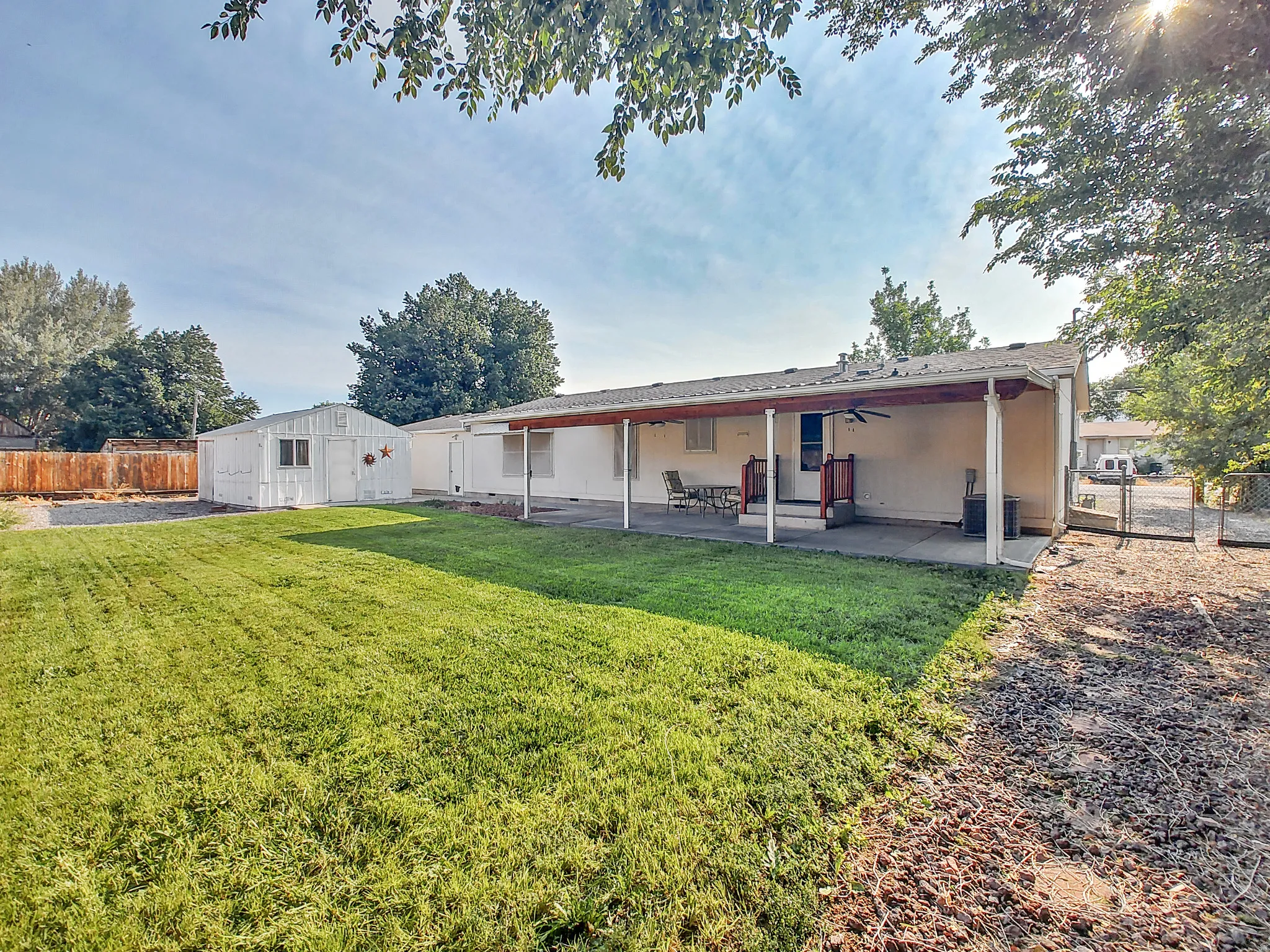 Expansive backyard featuring a manicured lawn, a large covered patio with ceiling fan, an additional storage shed, and a fenced area