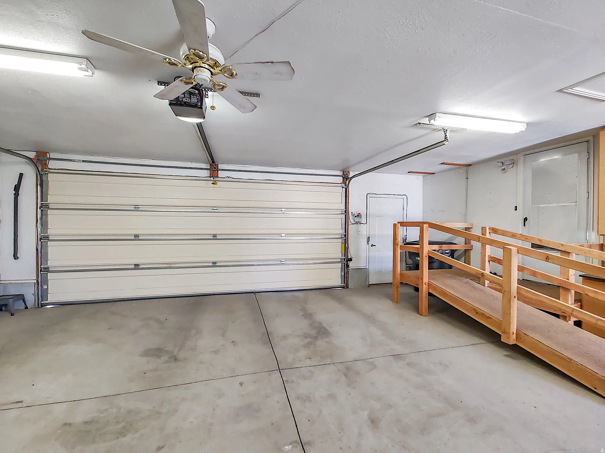 Spacious garage featuring a large overhead door, concrete flooring, fluorescent lighting, a ceiling fan, and a built-in wooden ramp