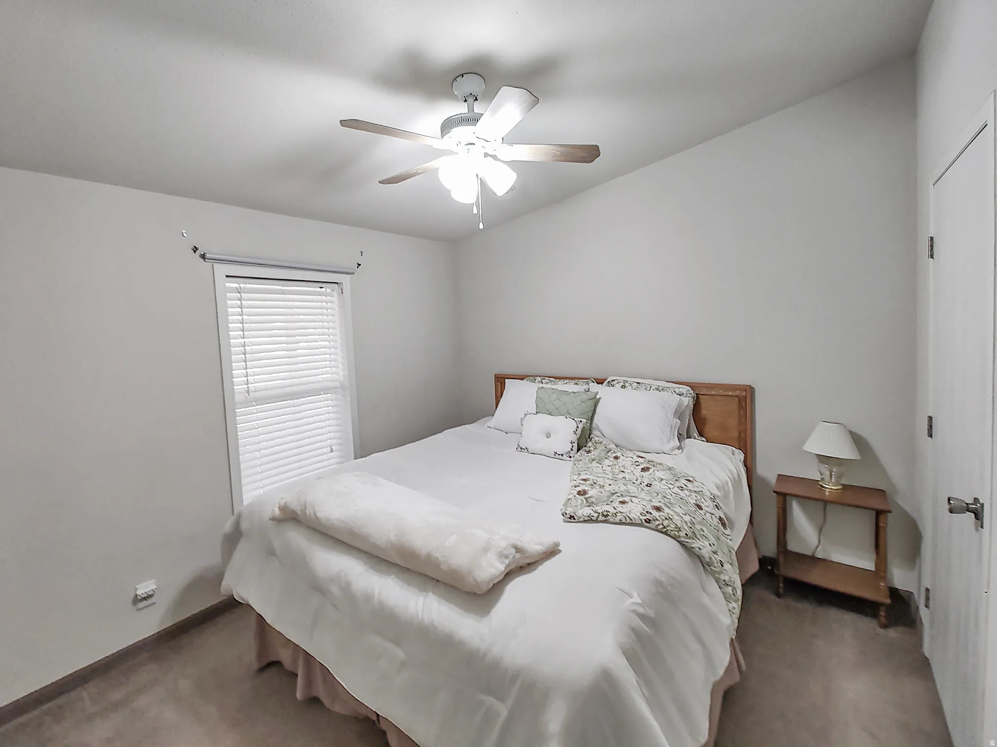 Vaulted ceiling bedroom featuring a ceiling fan with integrated lighting, a window with horizontal blinds, and a paneled door