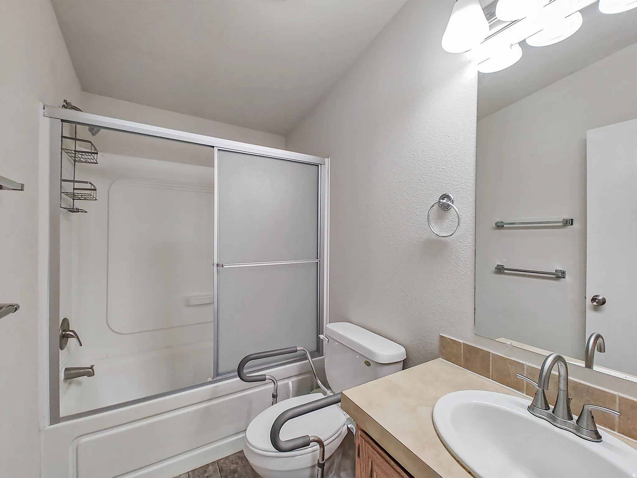 Bathroom featuring a bathtub with sliding glass doors, a vanity with an integrated sink, a rectangular mirror, and textured wall finish