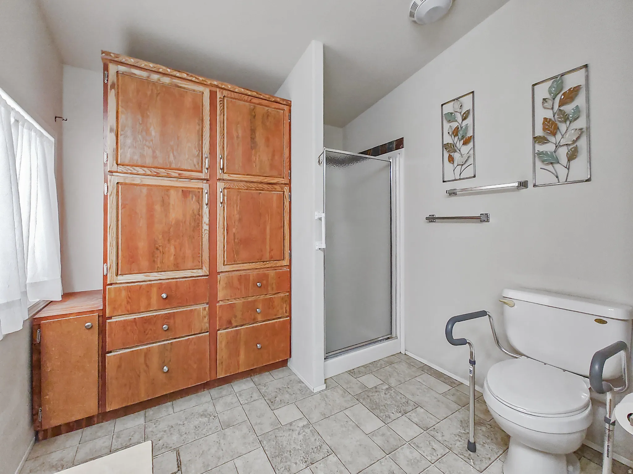 Primary Bathroom featuring a walk-in shower with frameless glass enclosure, dual vanity with matte black fixtures, tile flooring, and decorative wall art