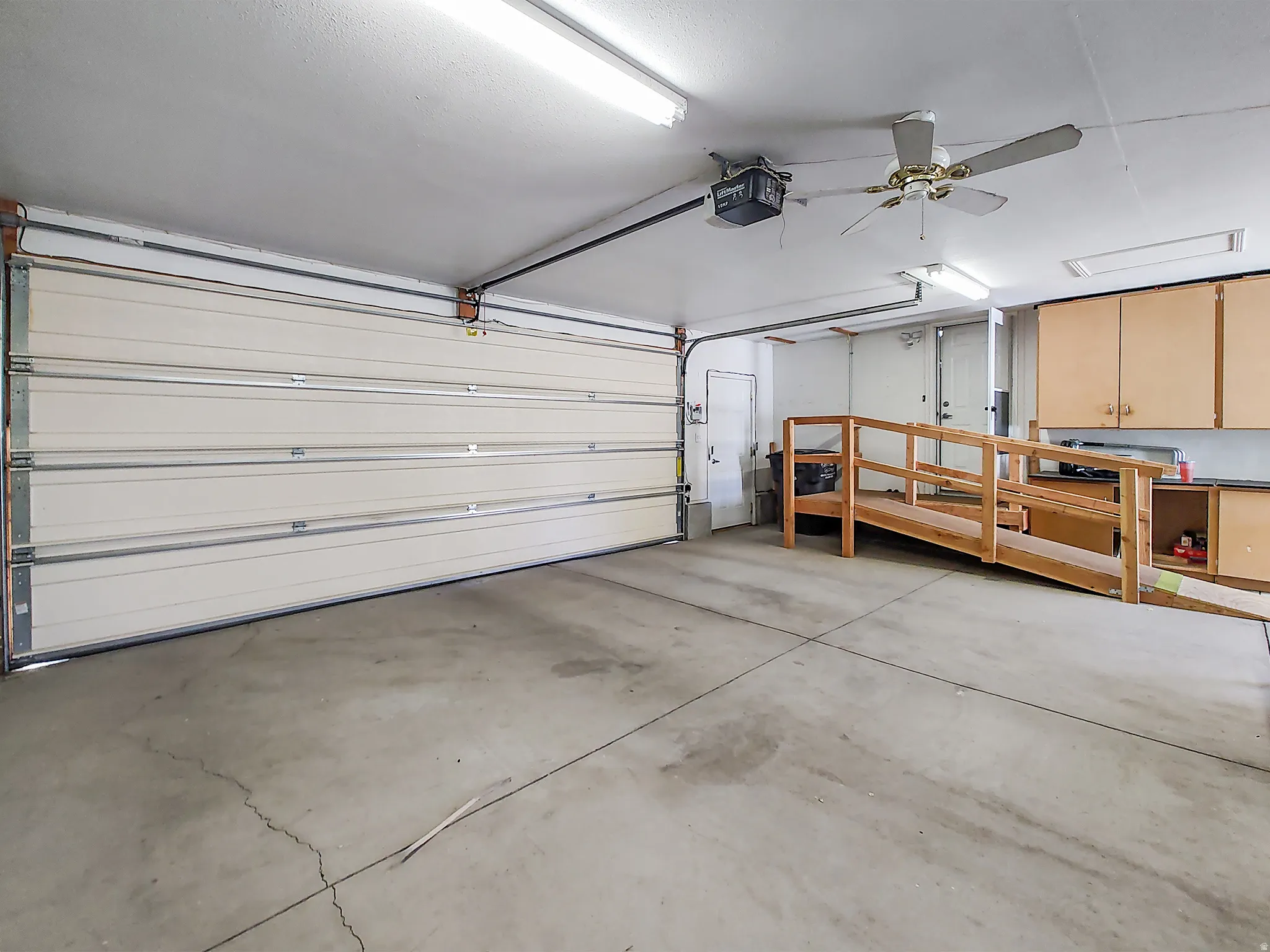 Spacious garage featuring a concrete floor, overhead fluorescent lighting, and a ceiling fan