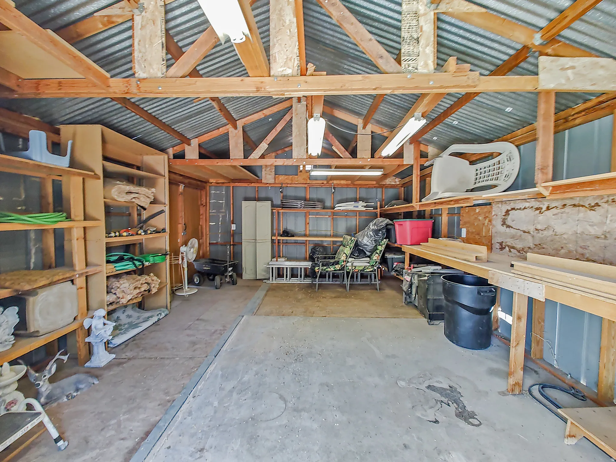 Interior of large storage shed in backyard with shelving and lighting.