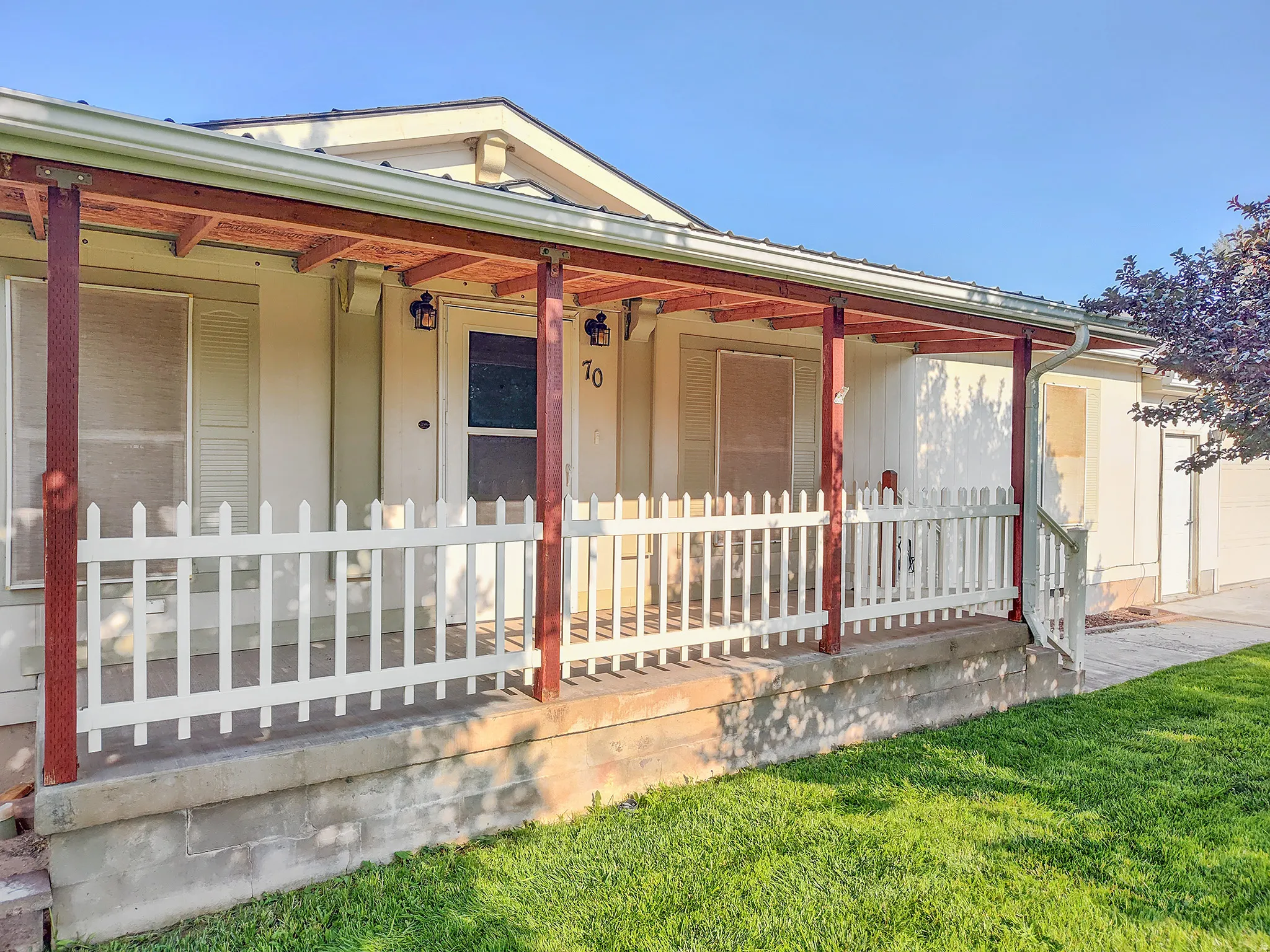 Front exterior featuring a covered porch with a white picket fence, wood-stained support beams, and exterior lighting fixtures