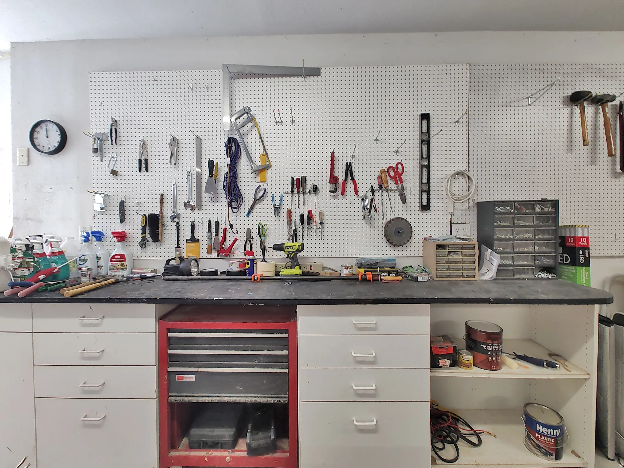Built-in workbench and tool storage in garage featuring expansive pegboard storage, integrated countertop, white cabinetry with multiple drawers, and open shelving