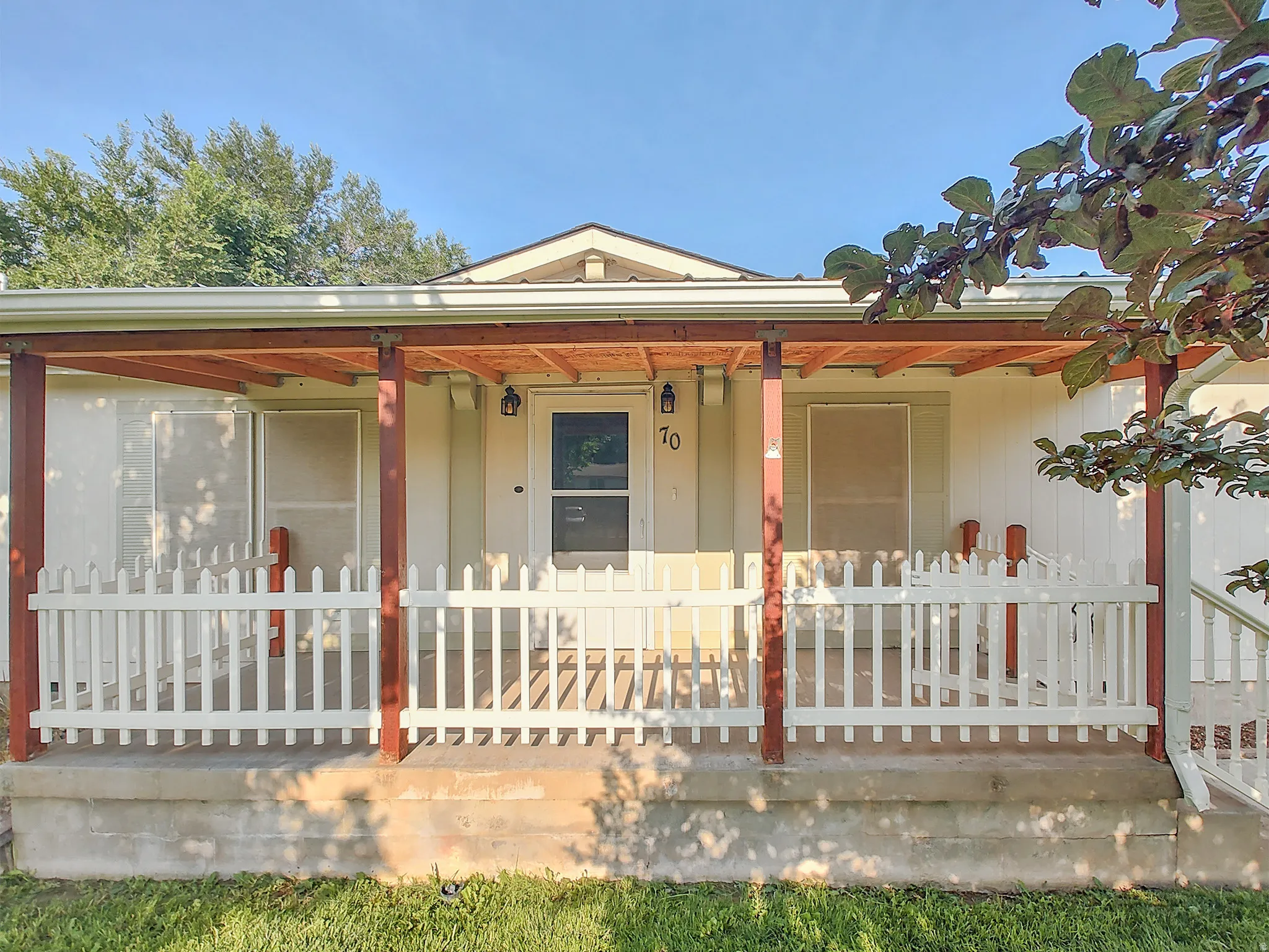 Covered front porch with white picket railing, wood-toned support beams, and exposed rafter ceiling