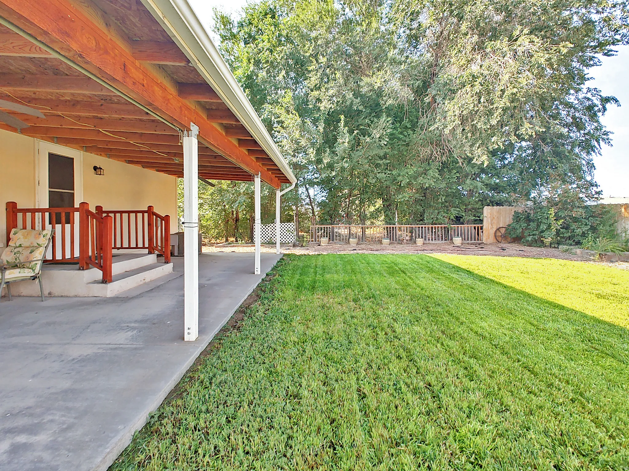 Expansive backyard retreat featuring a meticulously manicured lawn, mature tree-lined perimeter, and a covered patio with wooden beam construction