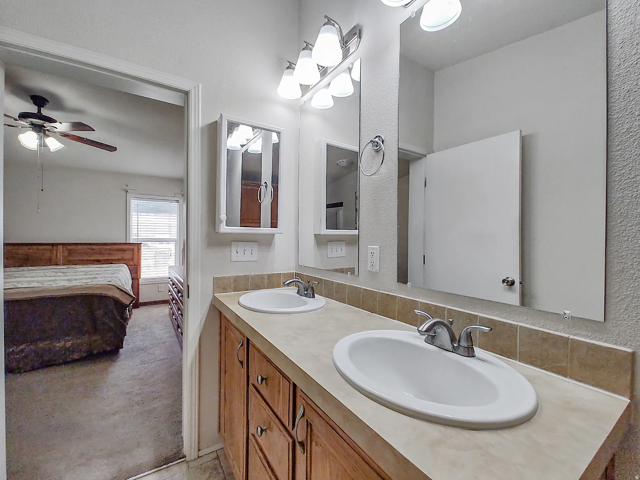 Double vanity featuring integrated sinks, ample countertop space, wood-finish cabinetry, and a mirrored medicine cabinet