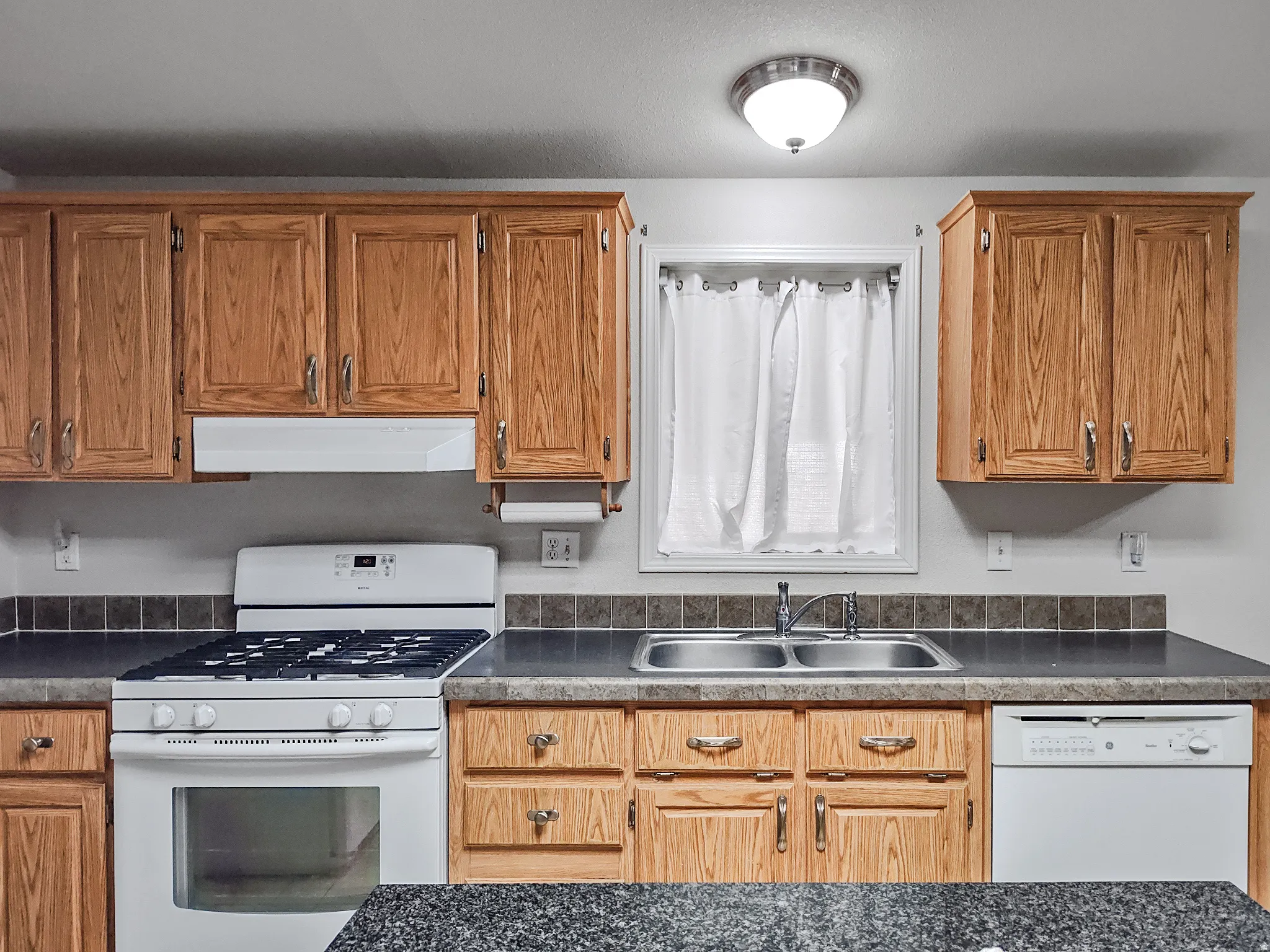 Kitchen featuring wood cabinetry, a double basin stainless steel sink, tile backsplash, and a white gas range with coordinating ventilation hood