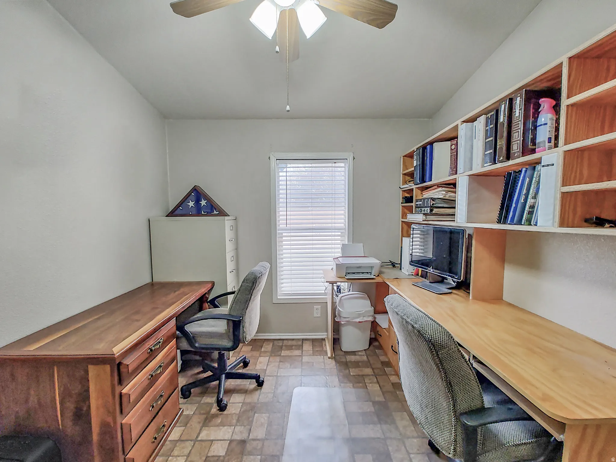 Bedroom or home office featuring dual wood-finish work surfaces with ample storage, built-in shelving throughout, ceiling fan with integrated lighting, and direct access to exterior door