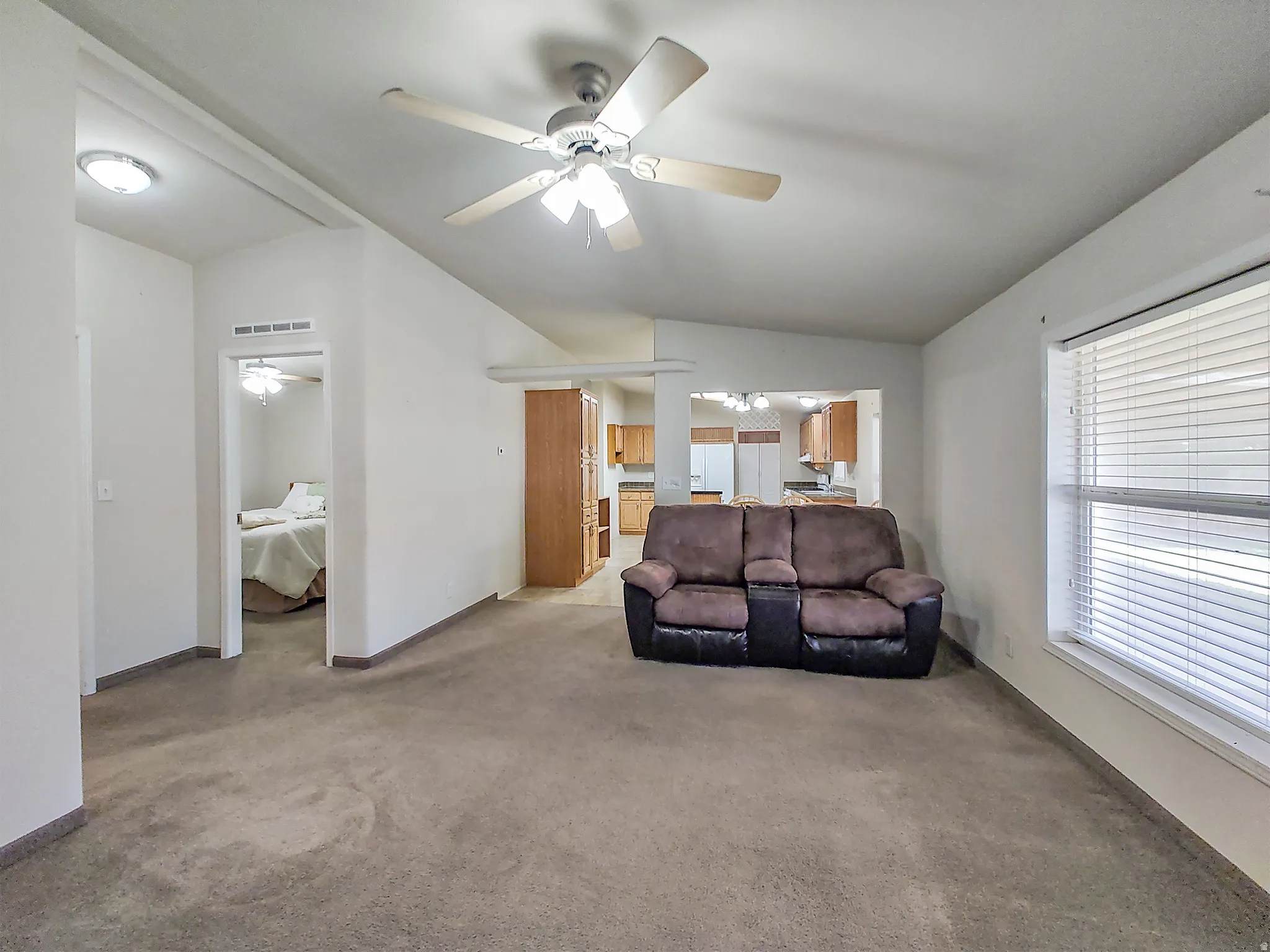 Open-concept living space featuring vaulted ceilings, ceiling fan light fixture, carpeted flooring, and a large window with blinds