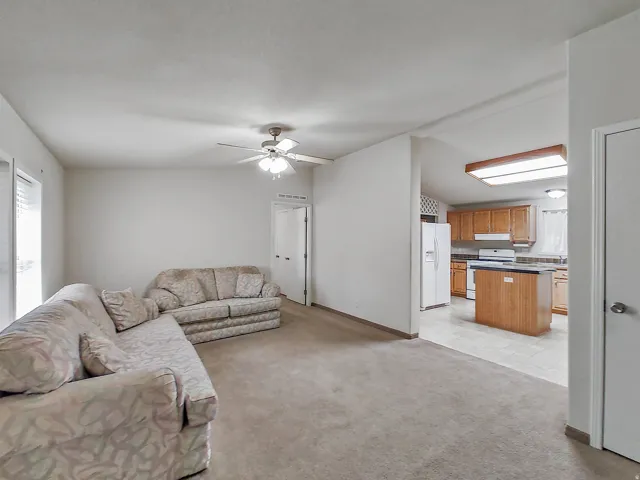Spacious living area with ceiling fan light fixture and carpet flooring