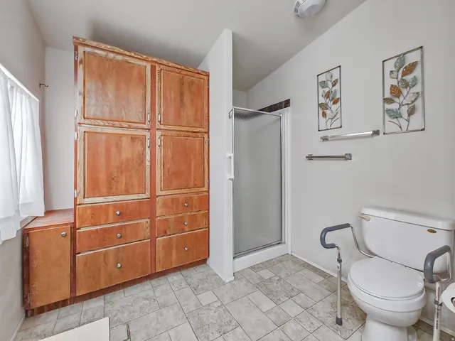 Primary Bathroom featuring a walk-in shower with frameless glass enclosure, dual vanity with matte black fixtures, tile flooring, and decorative wall art