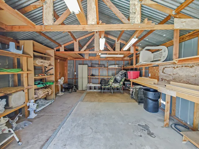 Interior of large storage shed in backyard with shelving and lighting.
