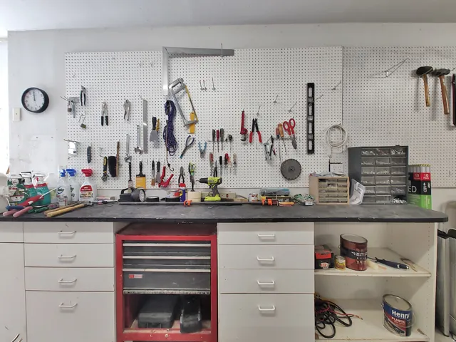 Built-in workbench and tool storage in garage featuring expansive pegboard storage, integrated countertop, white cabinetry with multiple drawers, and open shelving