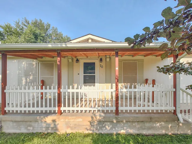 Covered front porch with white picket railing, wood-toned support beams, and exposed rafter ceiling