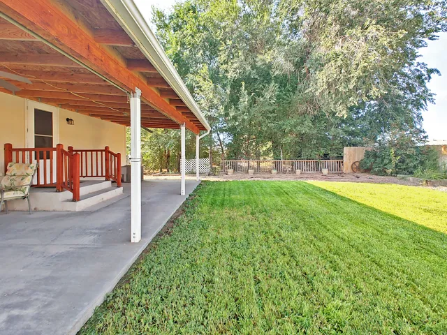 Expansive backyard retreat featuring a meticulously manicured lawn, mature tree-lined perimeter, and a covered patio with wooden beam construction