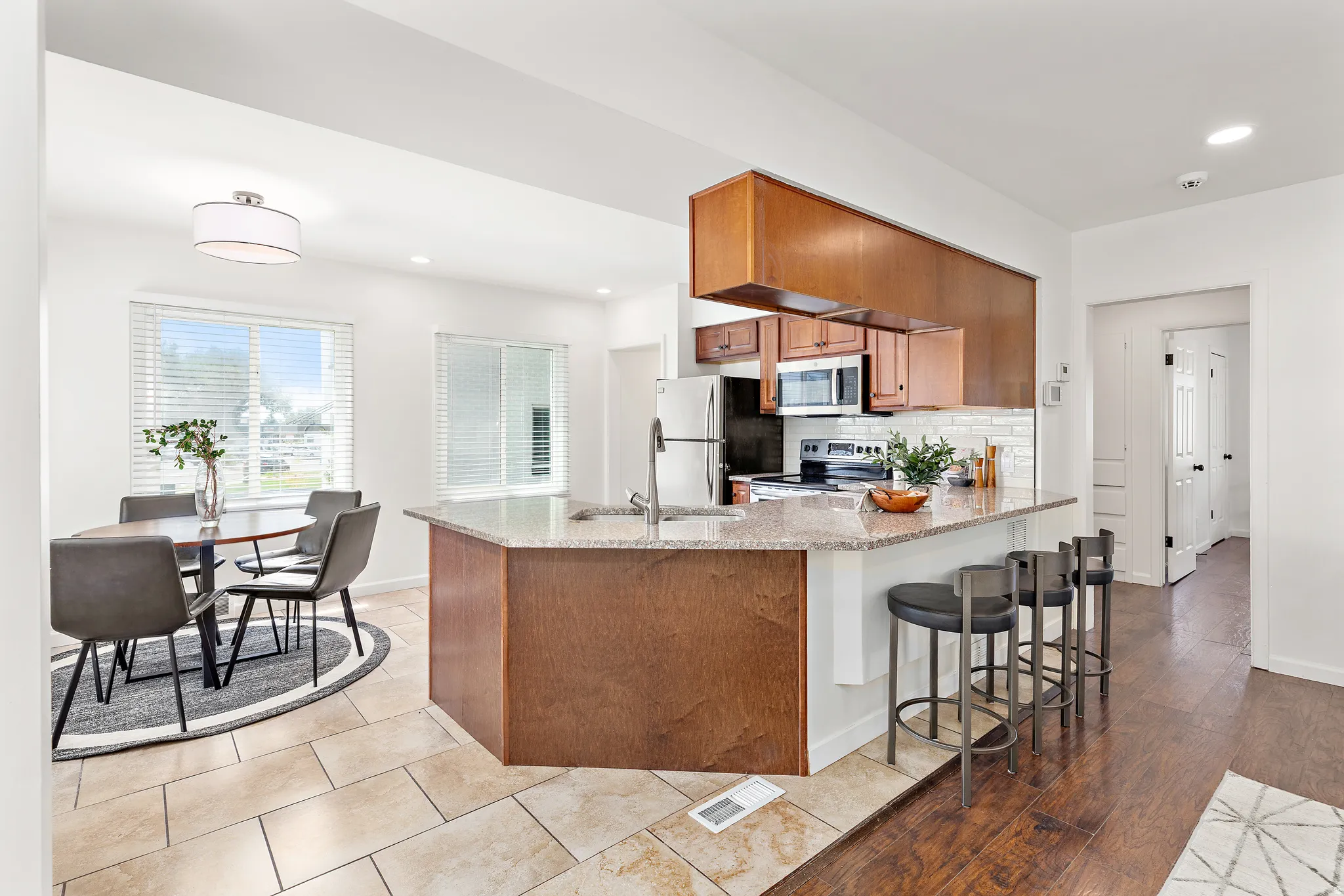 Open-concept kitchen and dining area featuring a breakfast bar with stone-finish countertop, wood cabinetry, and stainless steel appliances