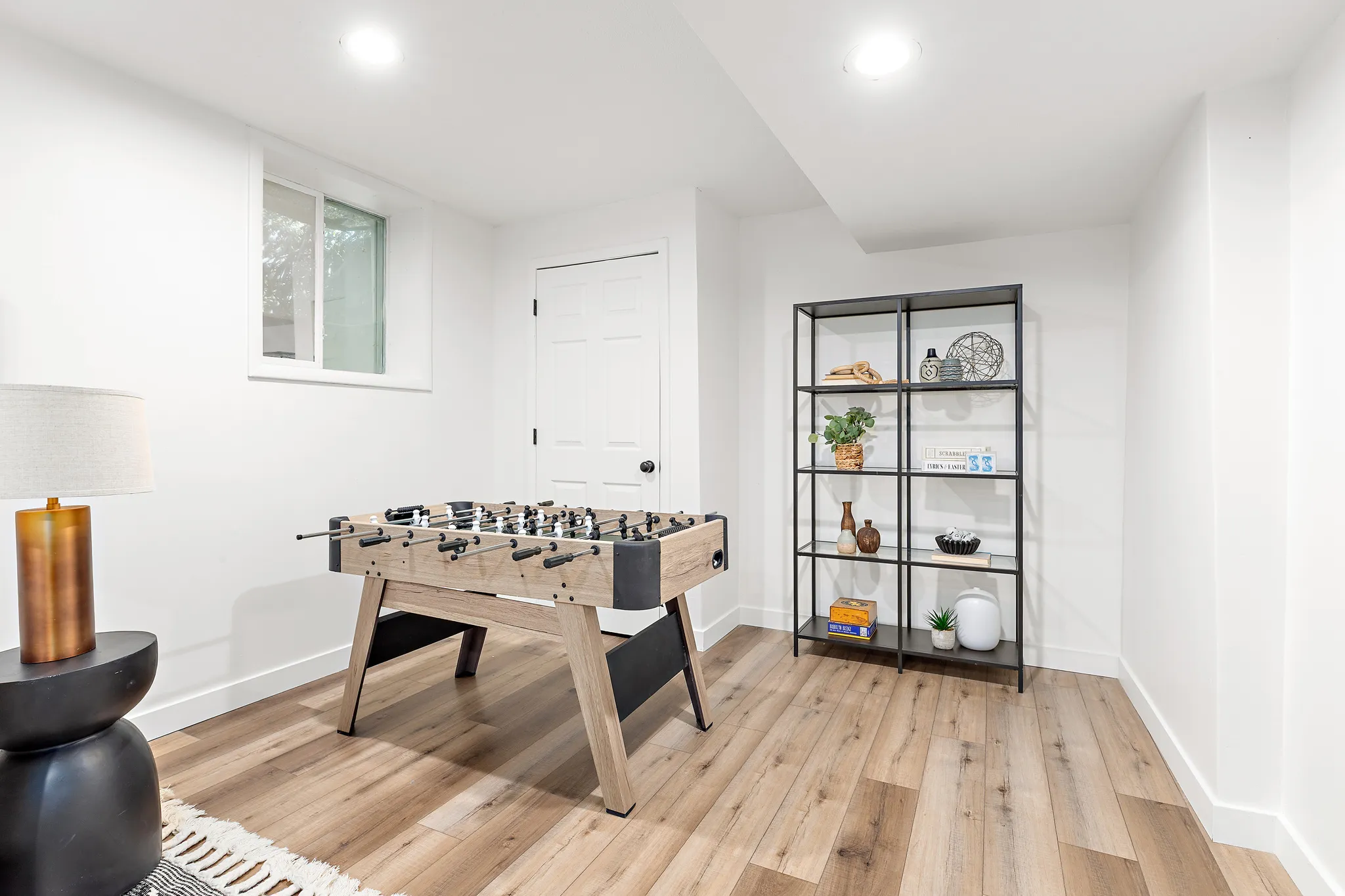 Finished lower level space featuring wood-finish flooring, recessed lighting, a white painted door, and a horizontal window