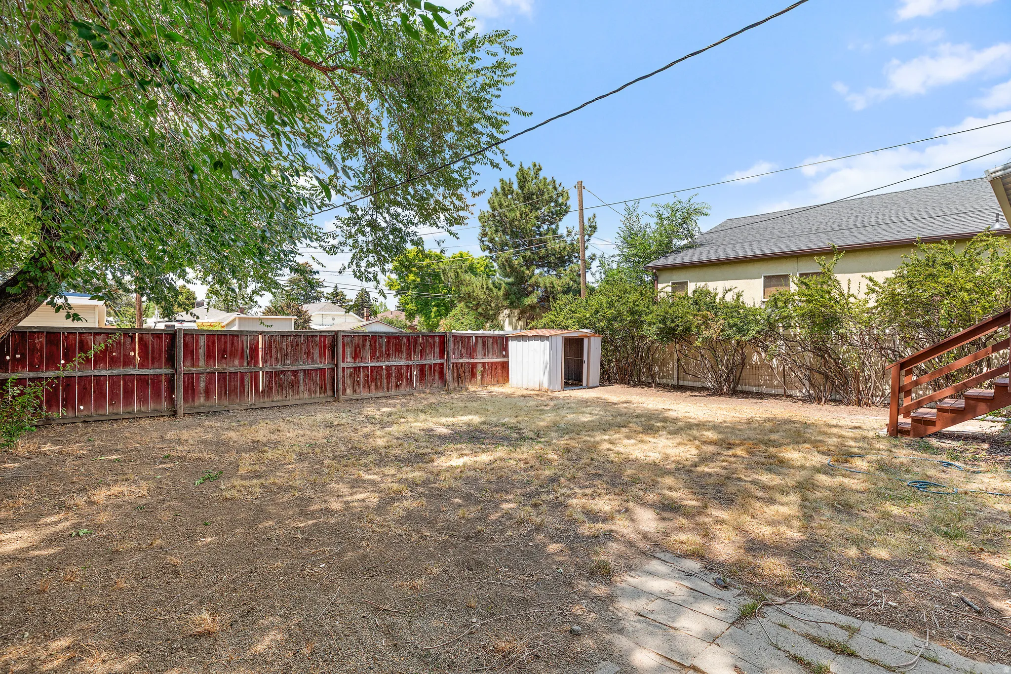 Expansive backyard featuring a solid wood fence, mature tree, and storage shed