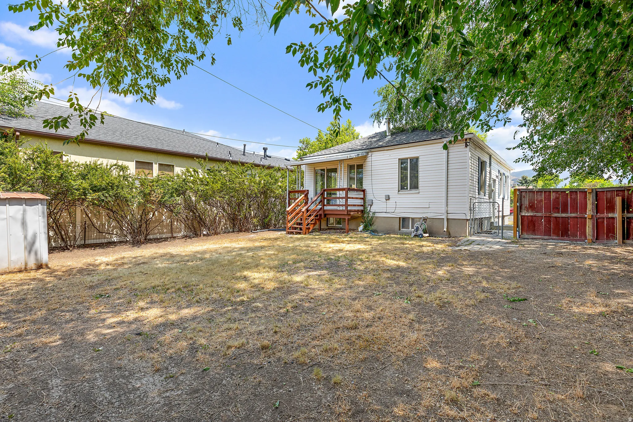 Expansive rear yard featuring a white siding exterior, wood deck, and partial red-toned fencing