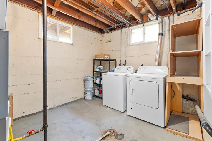 Dedicated laundry area featuring a white washing machine and dryer, exposed ceiling joists, concrete flooring, and multiple windows providing natural light