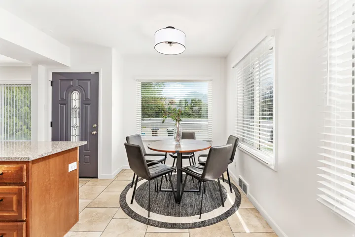 Bright dining area featuring tile flooring, multiple windows with blinds, a drum pendant light fixture, and a decorative front entry door with glass inserts