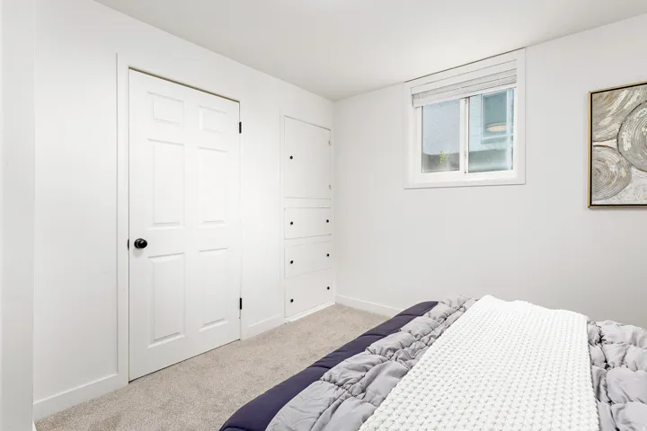Carpeted room featuring a double-pane window with blinds, a six-panel door, and built-in cabinetry with black hardware