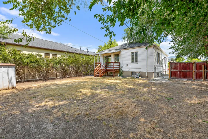 Expansive rear yard featuring a white siding exterior, wood deck, and partial red-toned fencing