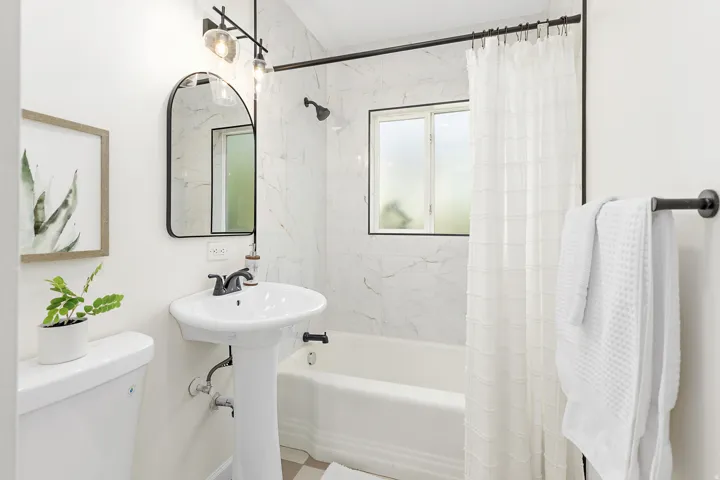 Bathroom featuring a pedestal sink, black-finish fixtures, an arched mirror, an integrated tub/shower with tile surround, and a frosted window