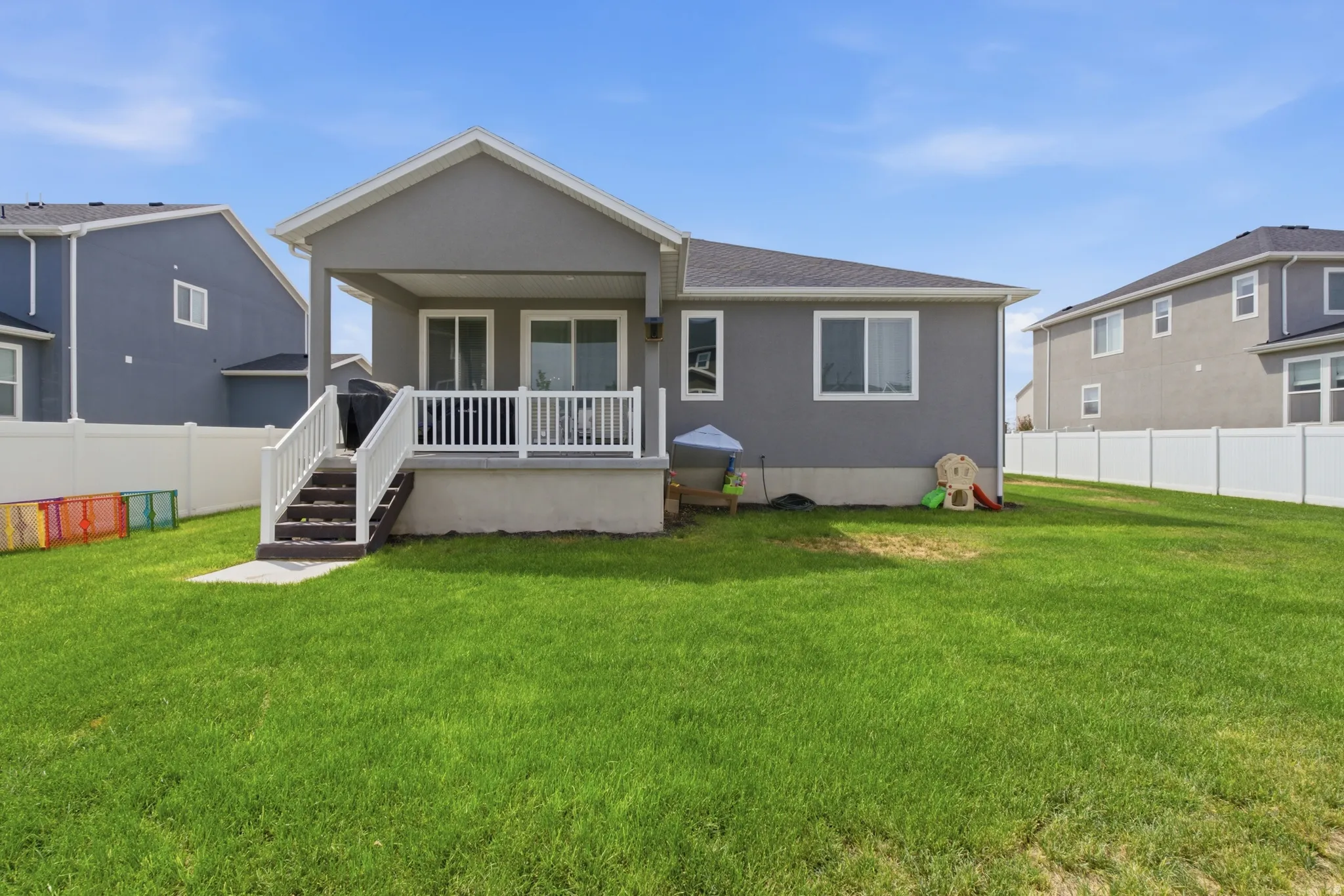 Expansive backyard with a manicured lawn, full white privacy fencing, and a covered patio with white railing