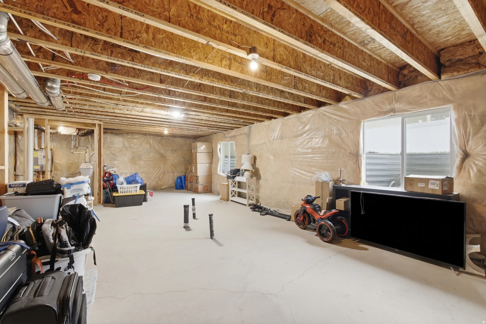 Unfinished lower level with exposed ceiling joists, concrete flooring, and a large egress window