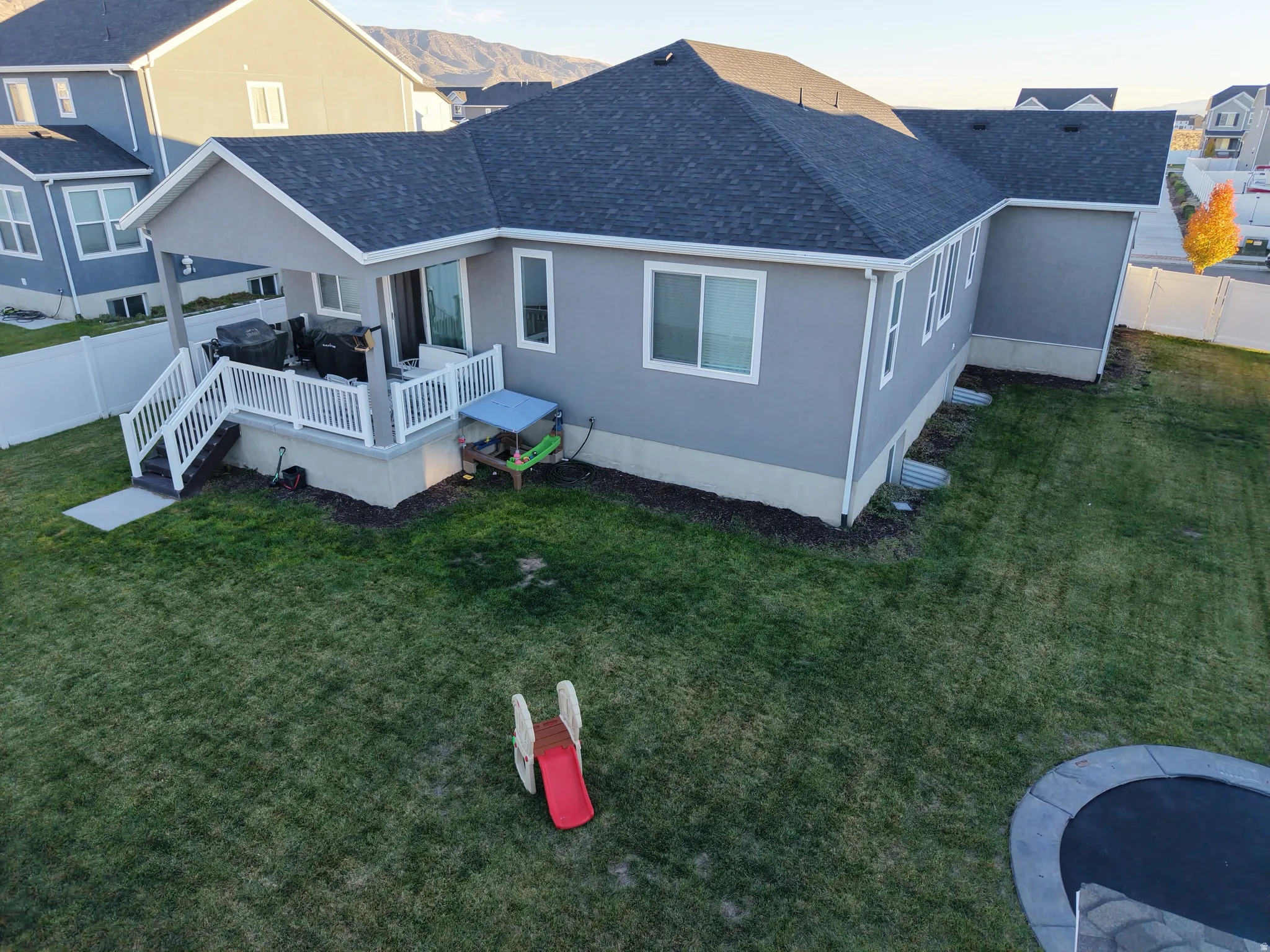 Rear exterior featuring a covered patio with white railings, a grey stucco finish, and a dark shingle roof