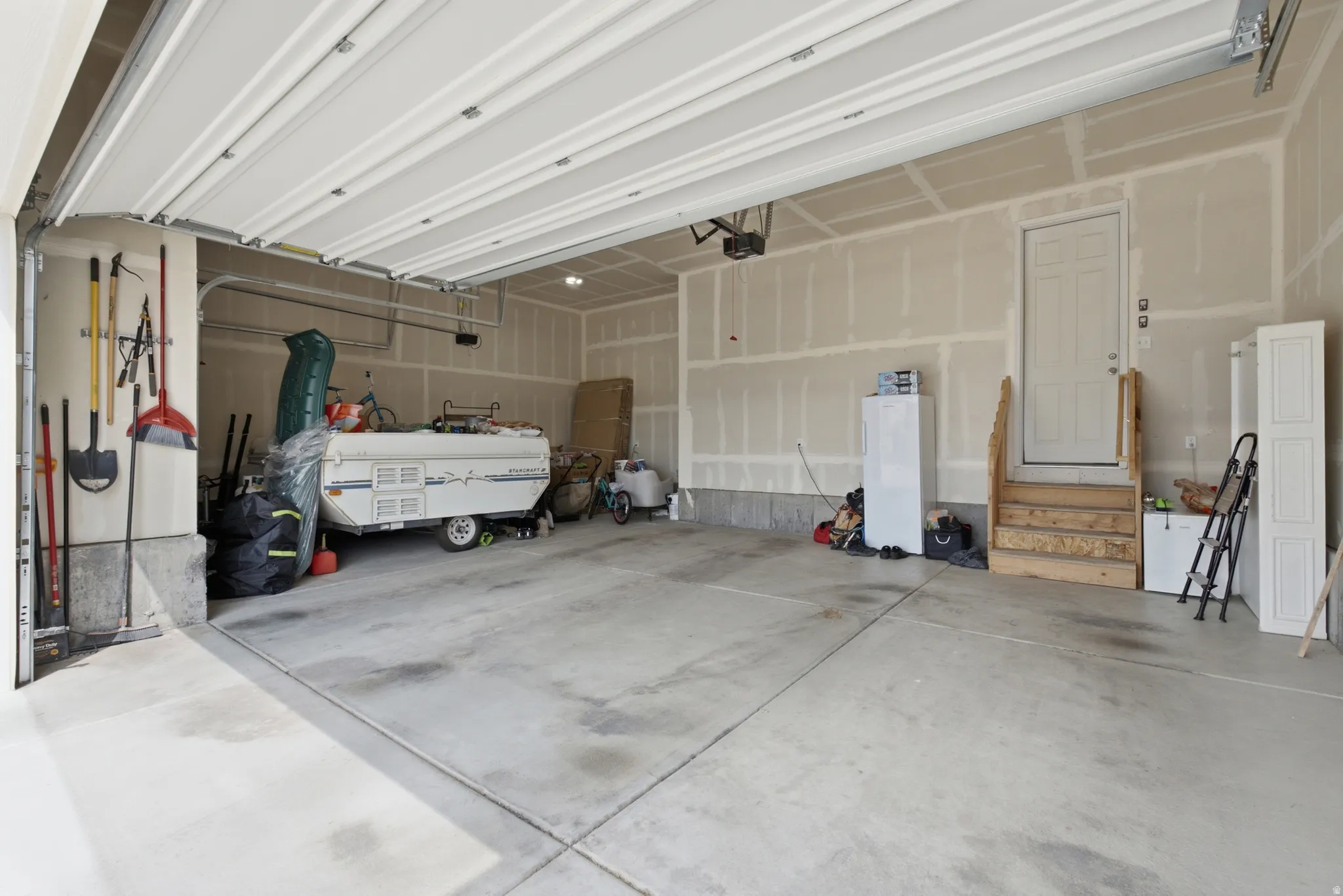 Attached garage with a concrete floor, overhead garage door, interior access door, and unpainted drywall walls