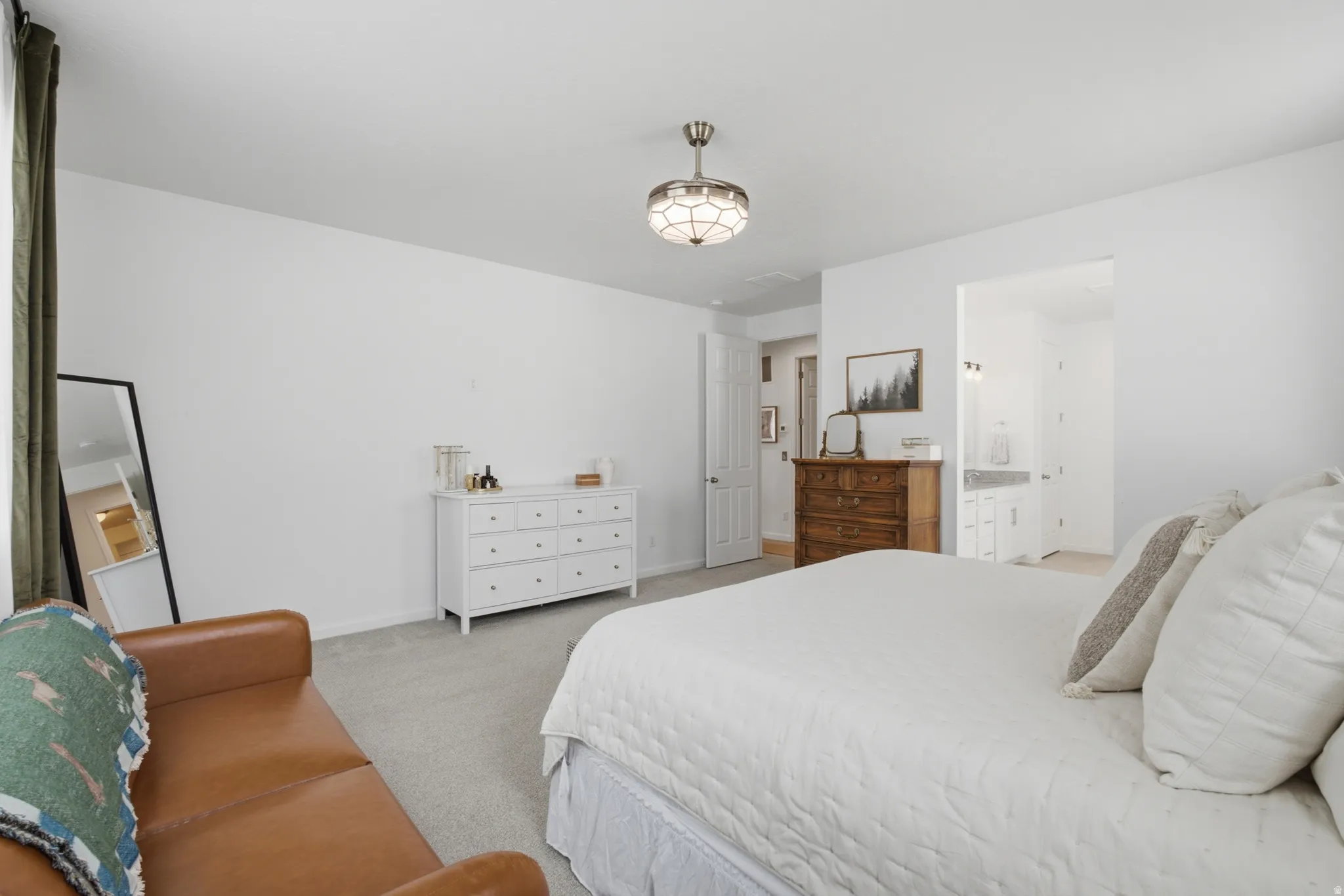 Neutral toned carpeting with a decorative ceiling fixture, white walls, and an open doorway revealing a vanity with a light-colored countertop