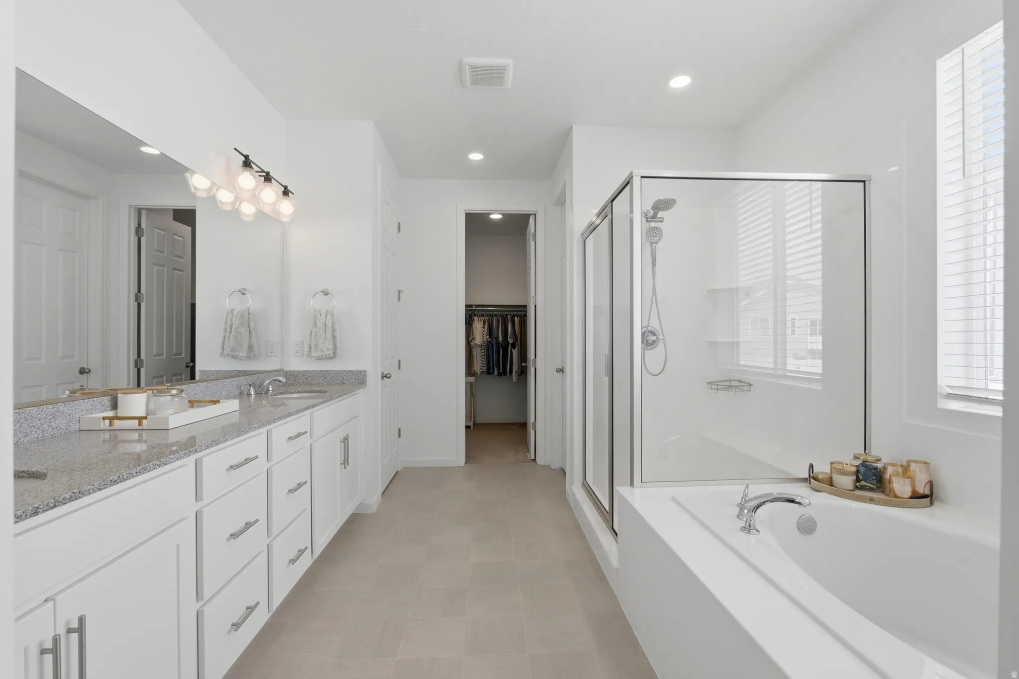 Dual vanity with light-toned countertop, glass-enclosed shower, built-in soaking tub, and tile flooring