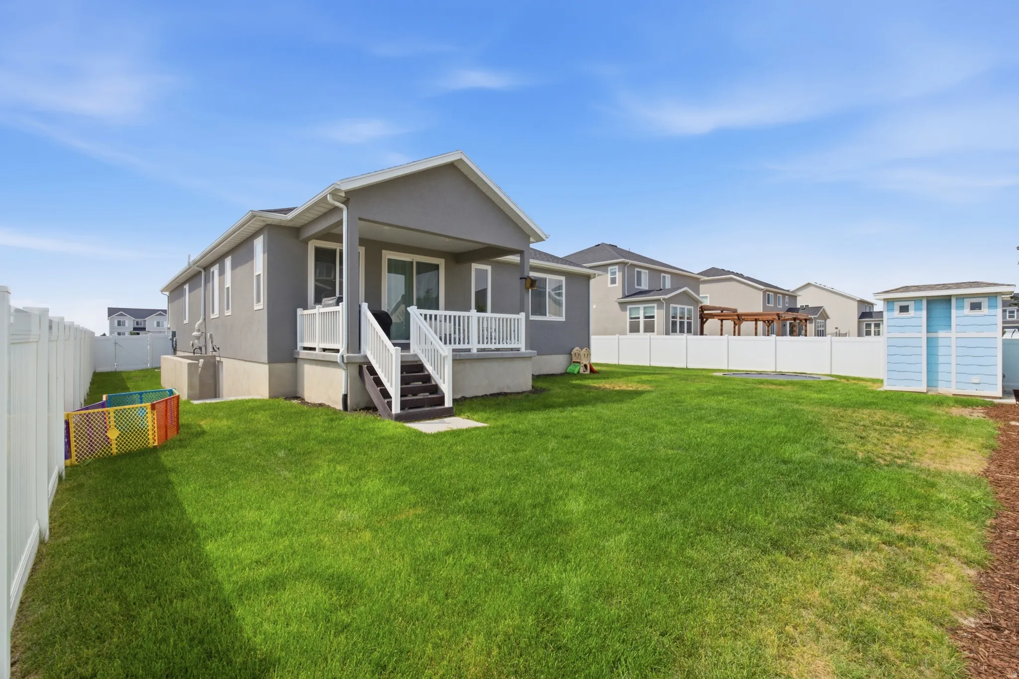 Expansive backyard featuring a manicured lawn, full fencing, a covered patio with white railing, and a blue storage shed