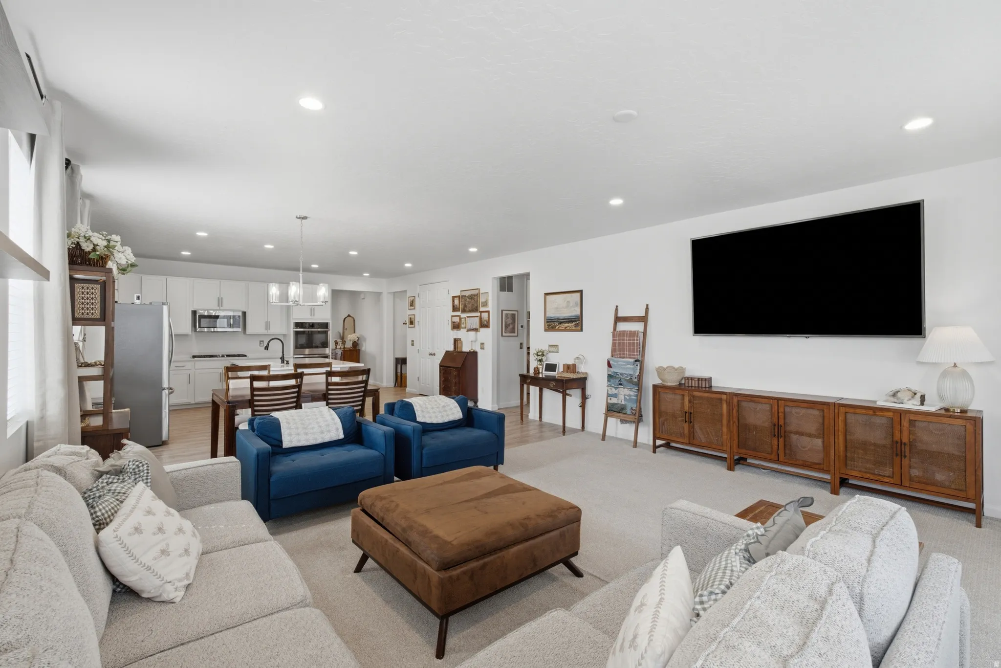 Recessed lighting throughout, light-toned wall finishes, and integrated kitchen with white cabinetry and stainless steel appliances