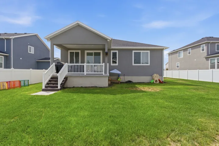Expansive backyard with a manicured lawn, full white privacy fencing, and a covered patio with white railing