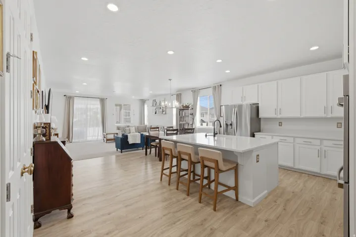 Open-concept kitchen and living area featuring wood-finish flooring, recessed lighting, a kitchen island with seating, and white cabinetry