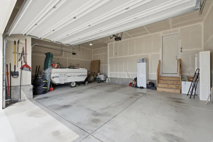 Attached garage with a concrete floor, overhead garage door, interior access door, and unpainted drywall walls
