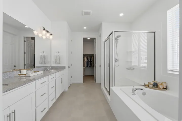 Dual vanity with light-toned countertop, glass-enclosed shower, built-in soaking tub, and tile flooring