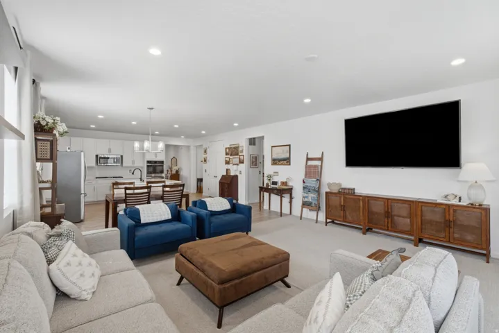 Recessed lighting throughout, light-toned wall finishes, and integrated kitchen with white cabinetry and stainless steel appliances