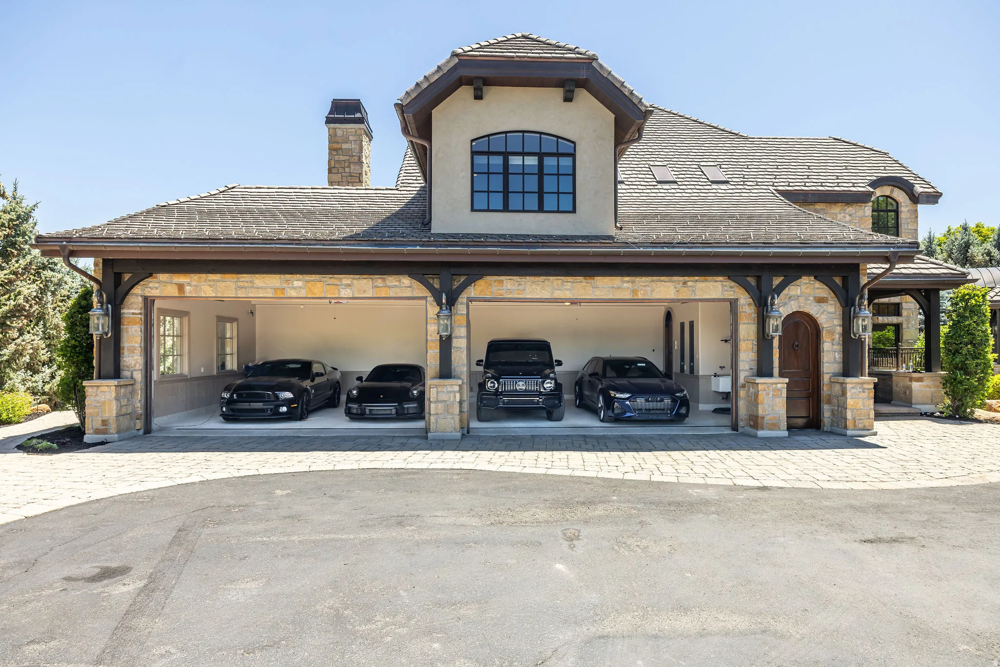 Four-bay garage with arched wooden supports, stone pillars, and exterior lighting
