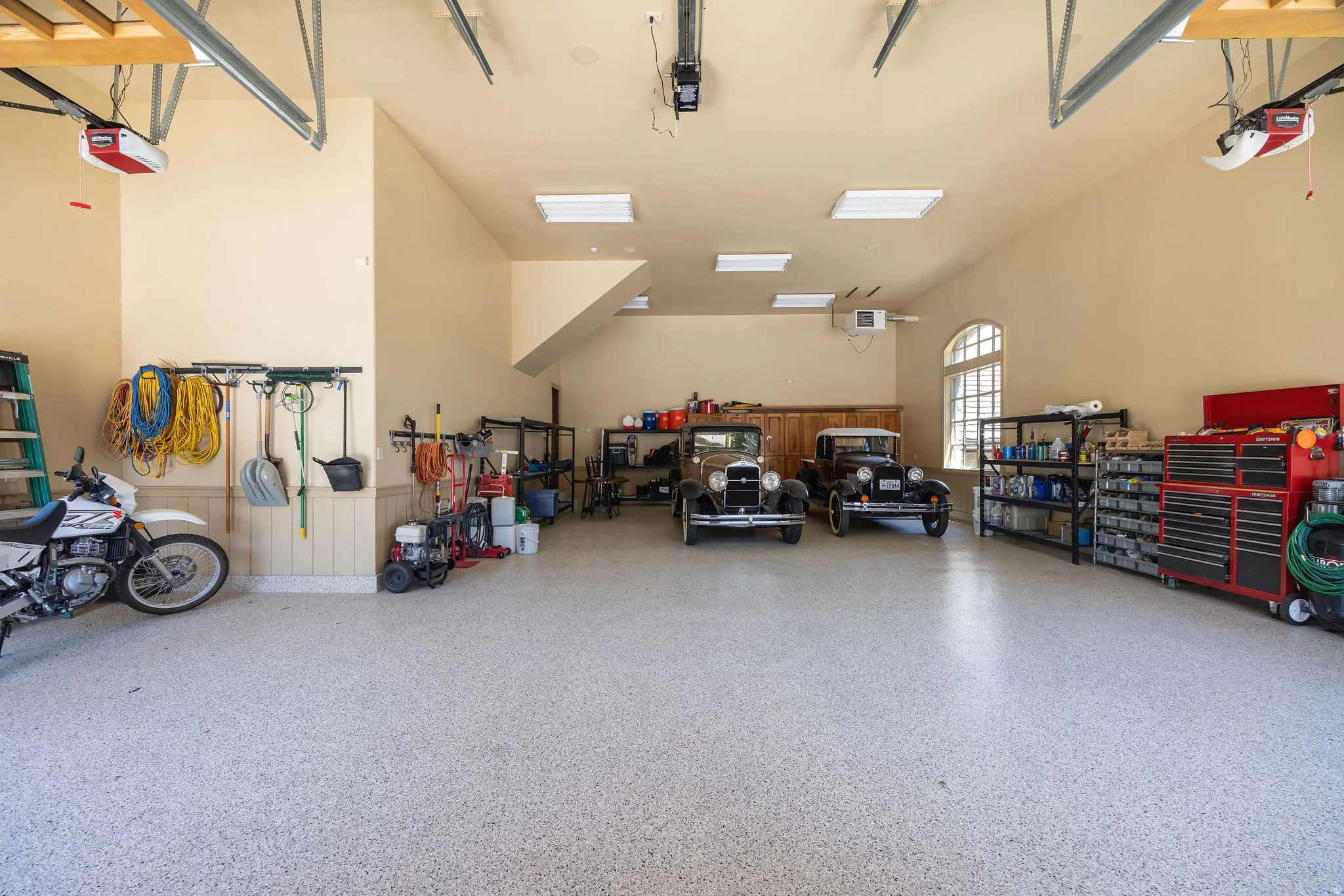 Spacious garage featuring a speckled epoxy flooring, vaulted ceilings, and dual automatic garage door openers