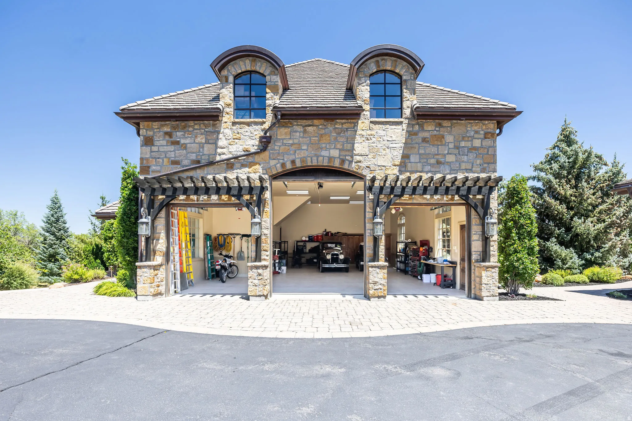 Stone exterior garage structure with multiple bays, an arched entry, two dormer windows, and a wood pergola