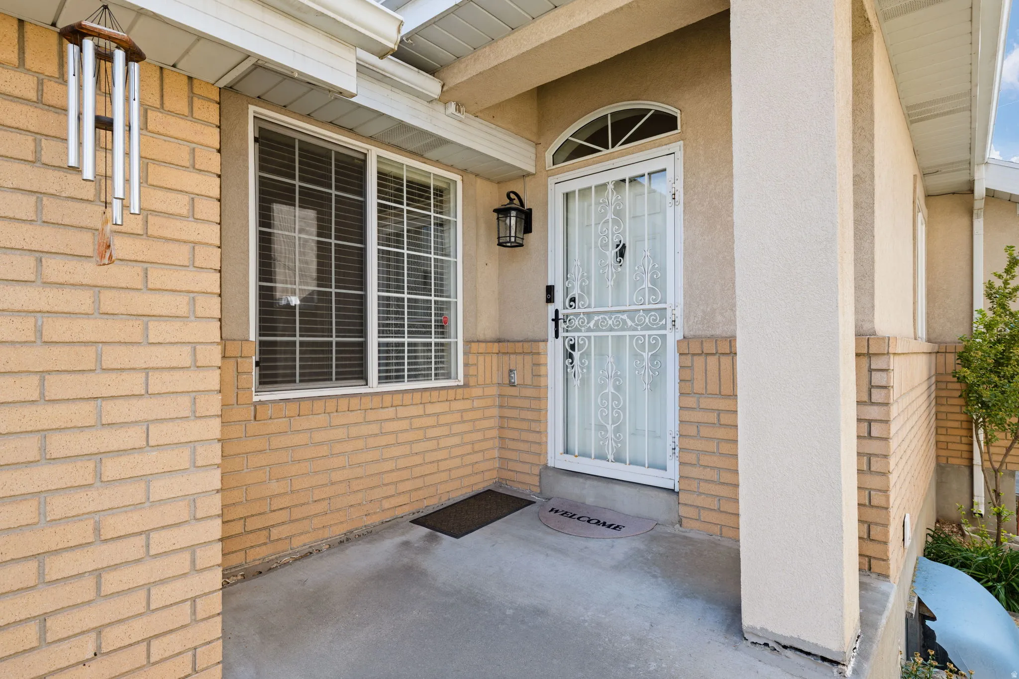 Brick and stucco exterior with a concrete porch, featuring a security screen door, an arched transom window, and an exterior wall light
