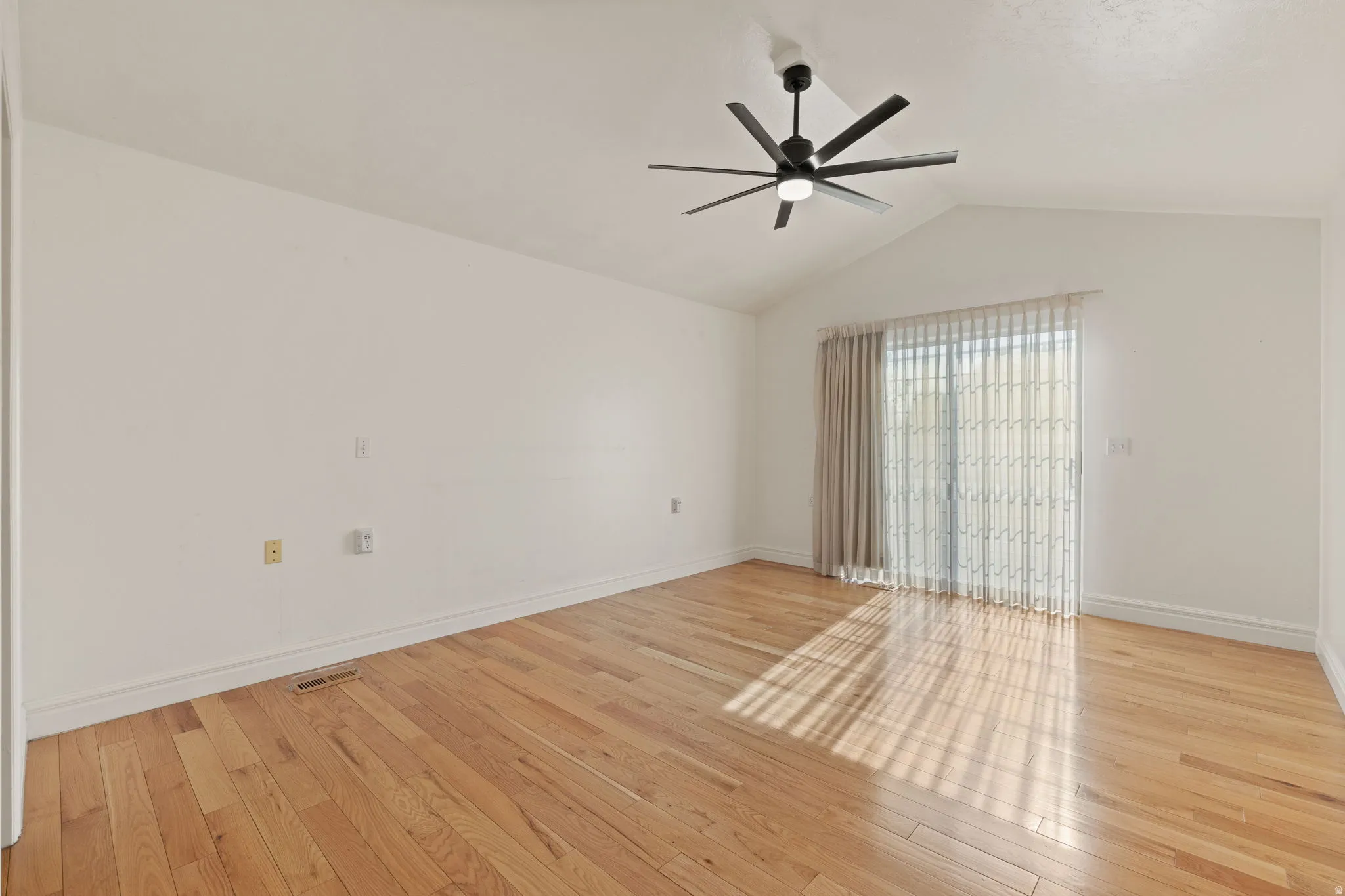 Vaulted ceiling, wood-finish flooring, modern ceiling fan, sliding glass door, white wall finishes